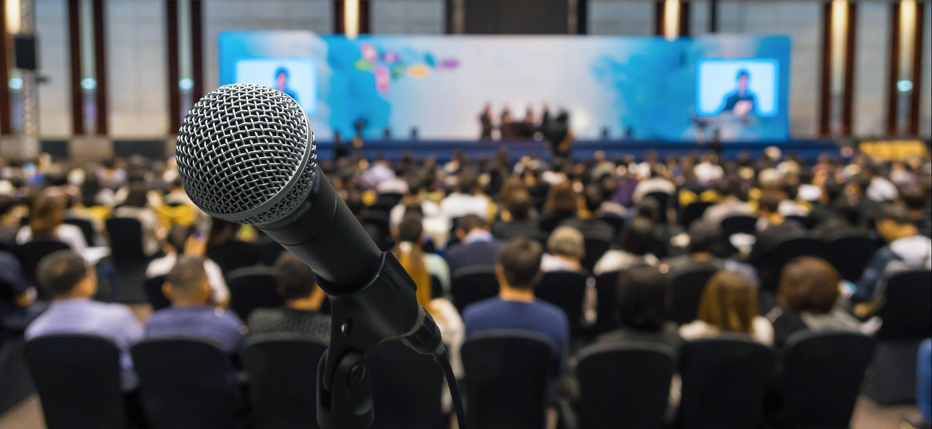 Sala konferencyjna wypełnioną ludźmi, na pierwszym planie jest mikrofon