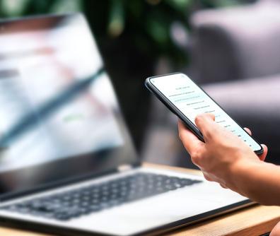 Laptop, ręka osoby trzymającej smartfona 