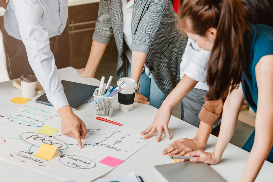 Grupa osób stojąca nad stołem, na którym rozłożone są dokumenty