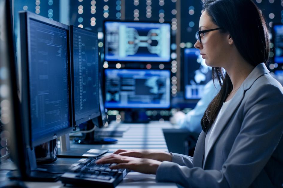Kobieta pracująca przy komputerze otoczona monitorami